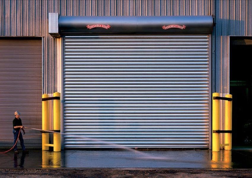 Closed metal storefront shutters at dusk, with a person walking past on the left.