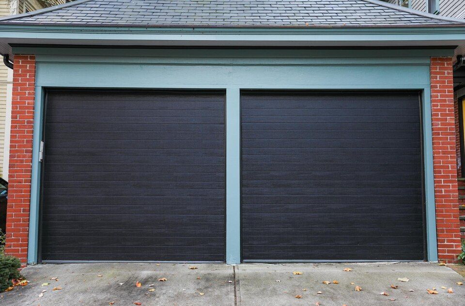Two black garage doors on a brick house with light blue trim and a concrete driveway