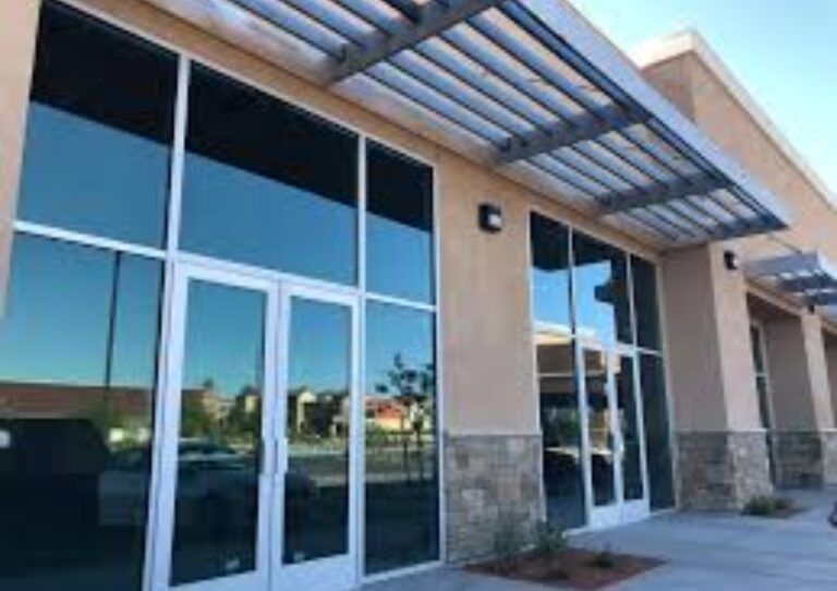 Modern storefront with glass doors, large windows, and a metal awning under clear blue sky