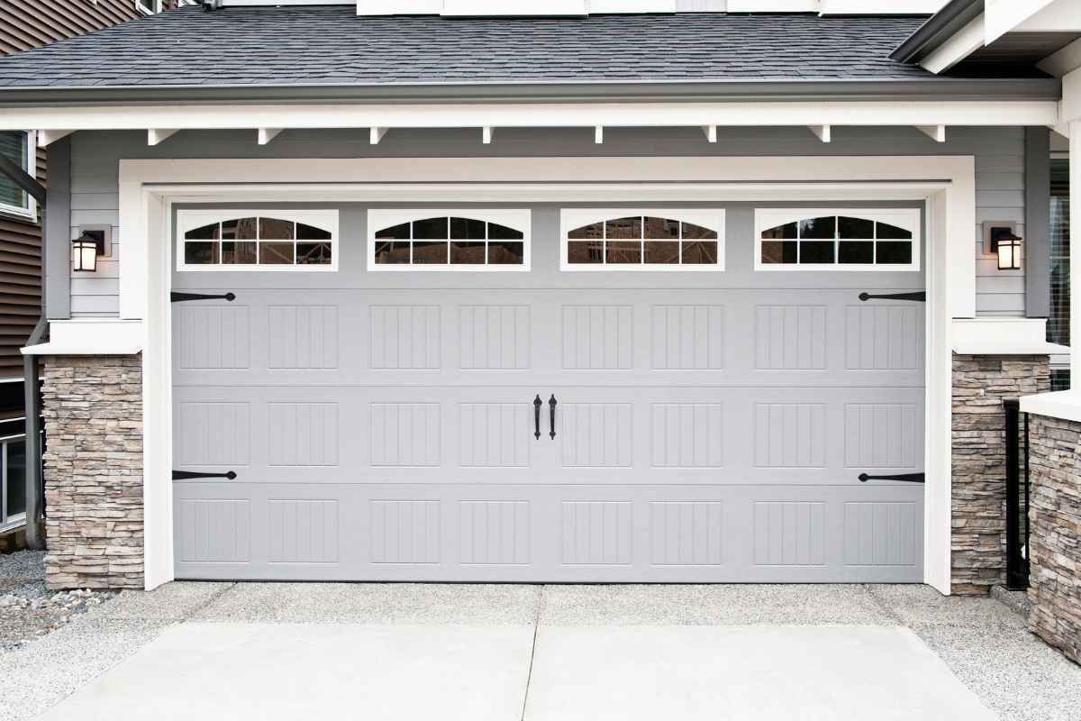 Light gray double garage door with black handles and stone trim on a house exterior