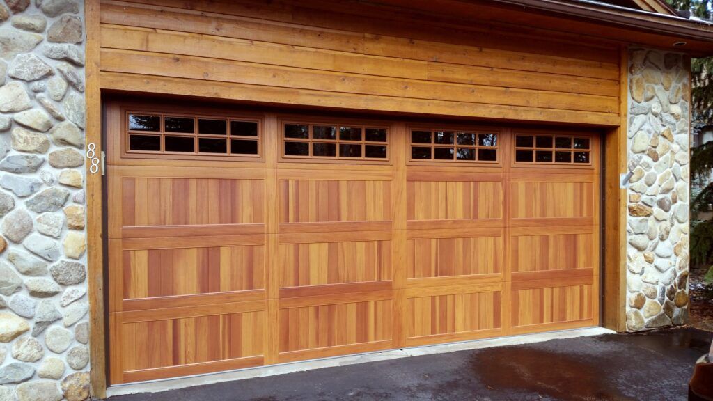 Wooden double garage doors with small windows set in a stone and wood exterior