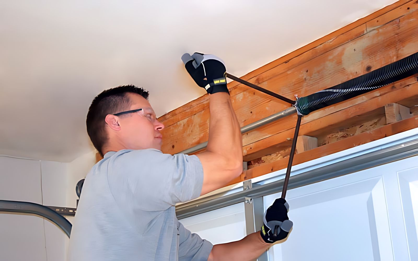 Person tightening a garage door opener rail with a wrench, standing on a ladder in a garage.