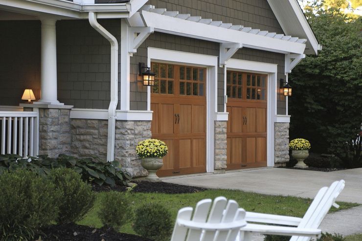 House entrance with wooden double doors, stone columns, and white porch chairs in front of a landscaped yard