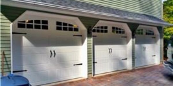 White three-car garage with arched windows and black handles on a house exterior