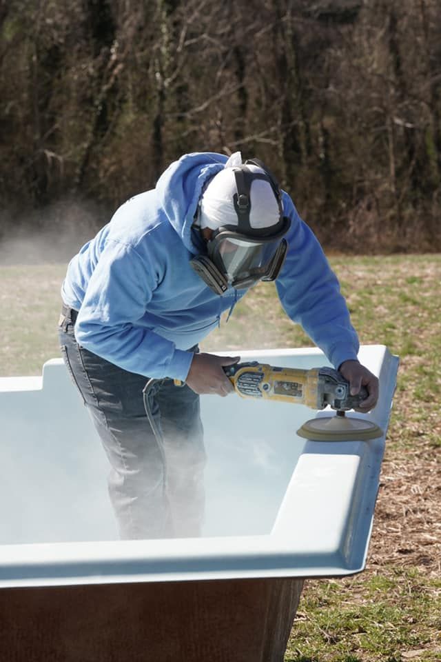 Person wearing protective gear grinds a surface inside a large tub, creating a cloud of dust.