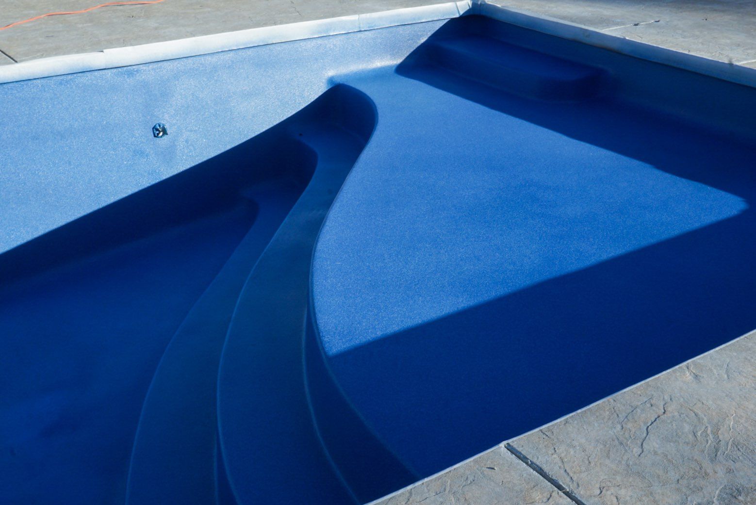 Blue swimming pool with steps, viewed from above.