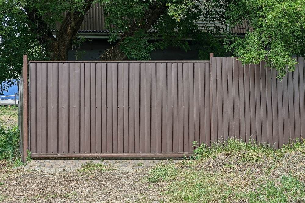 A Brown Fence is Surrounded by Trees and Grass in Front of a House — Downright Carpentry in Ryan, QLD