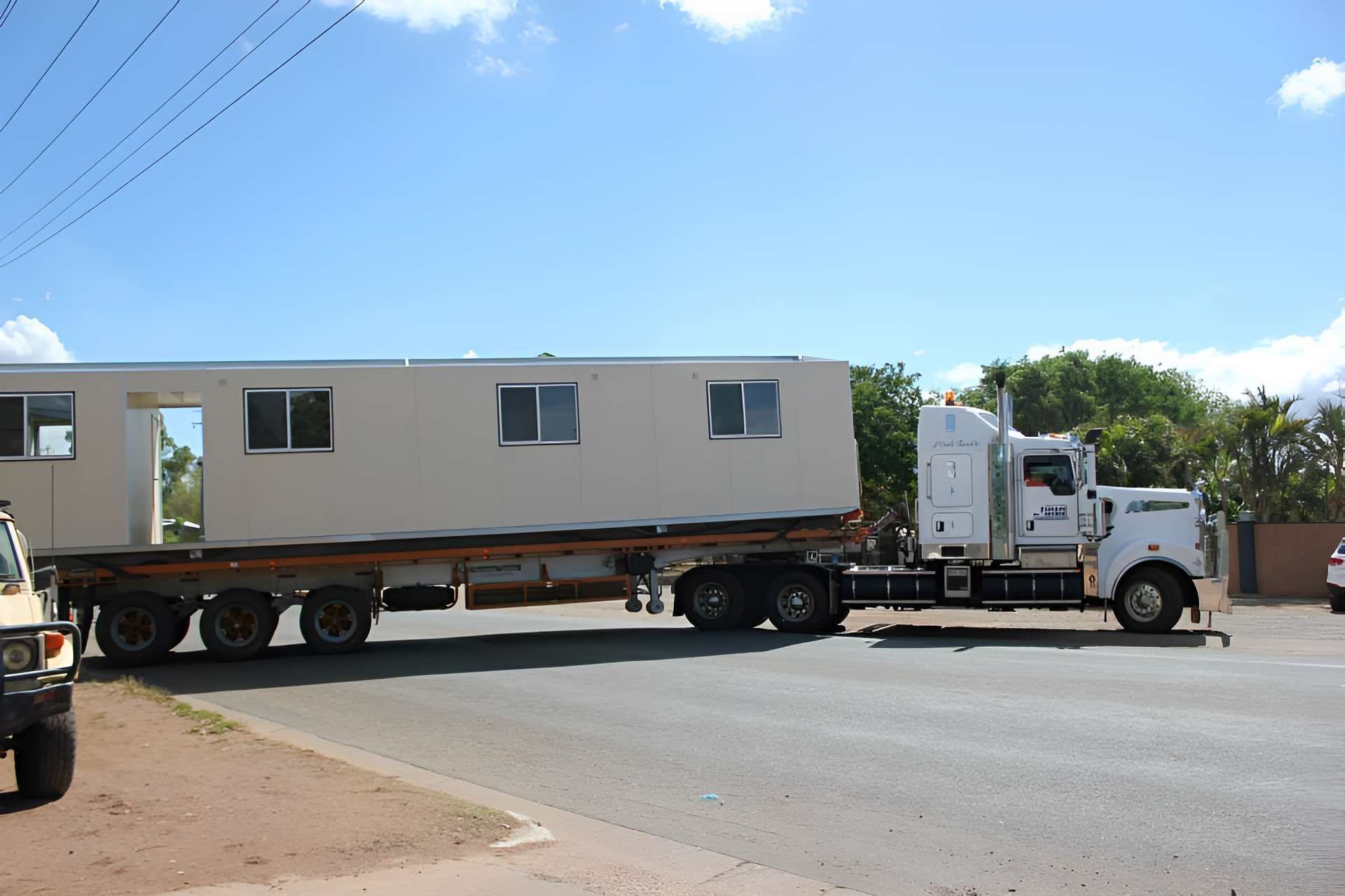 A White Semi Truck is Carrying a House on the Back of It — Downright Carpentry in Ryan, QLD