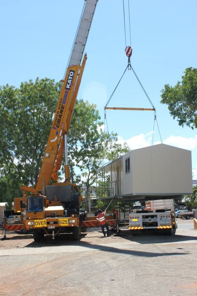 A Large Yellow Crane is Lifting a Container in a Parking Lot — Downright Carpentry in Ryan, QLD
