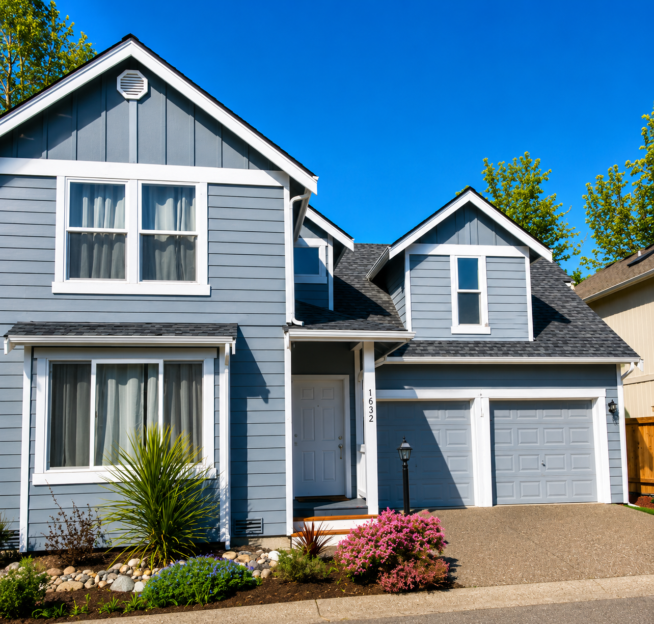 Gray suburban house with white trim, double garage, and a small front garden under a bright blue sky
