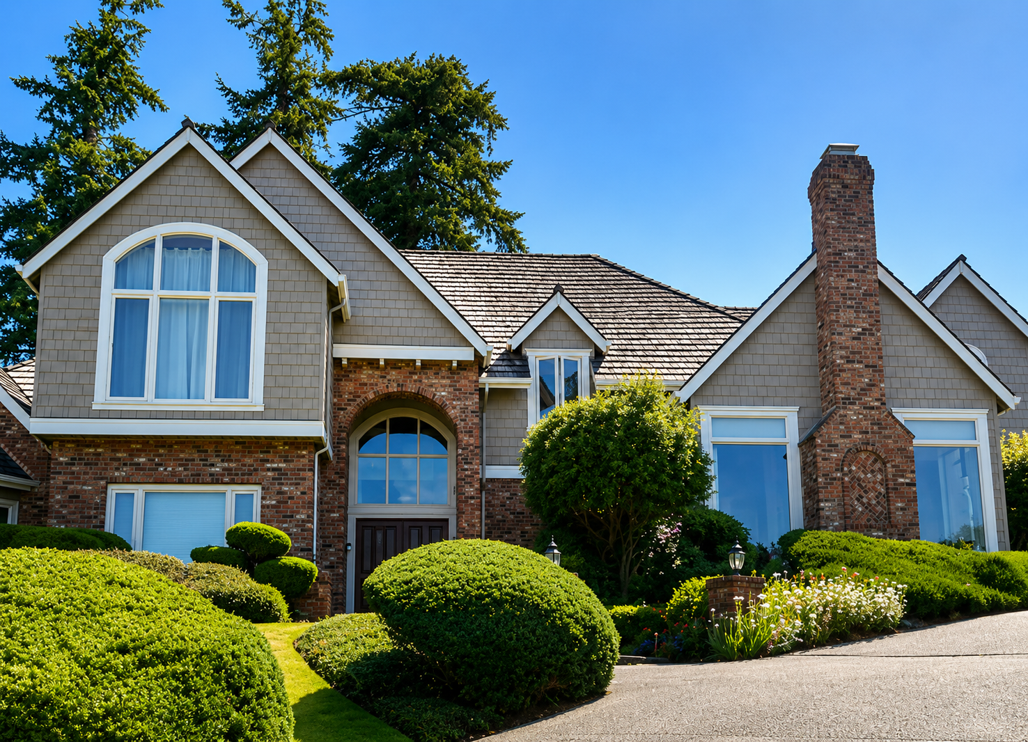 Large suburban house with stone facade, blue windows, arched entry, and neatly trimmed shrubs under a sunny sky
