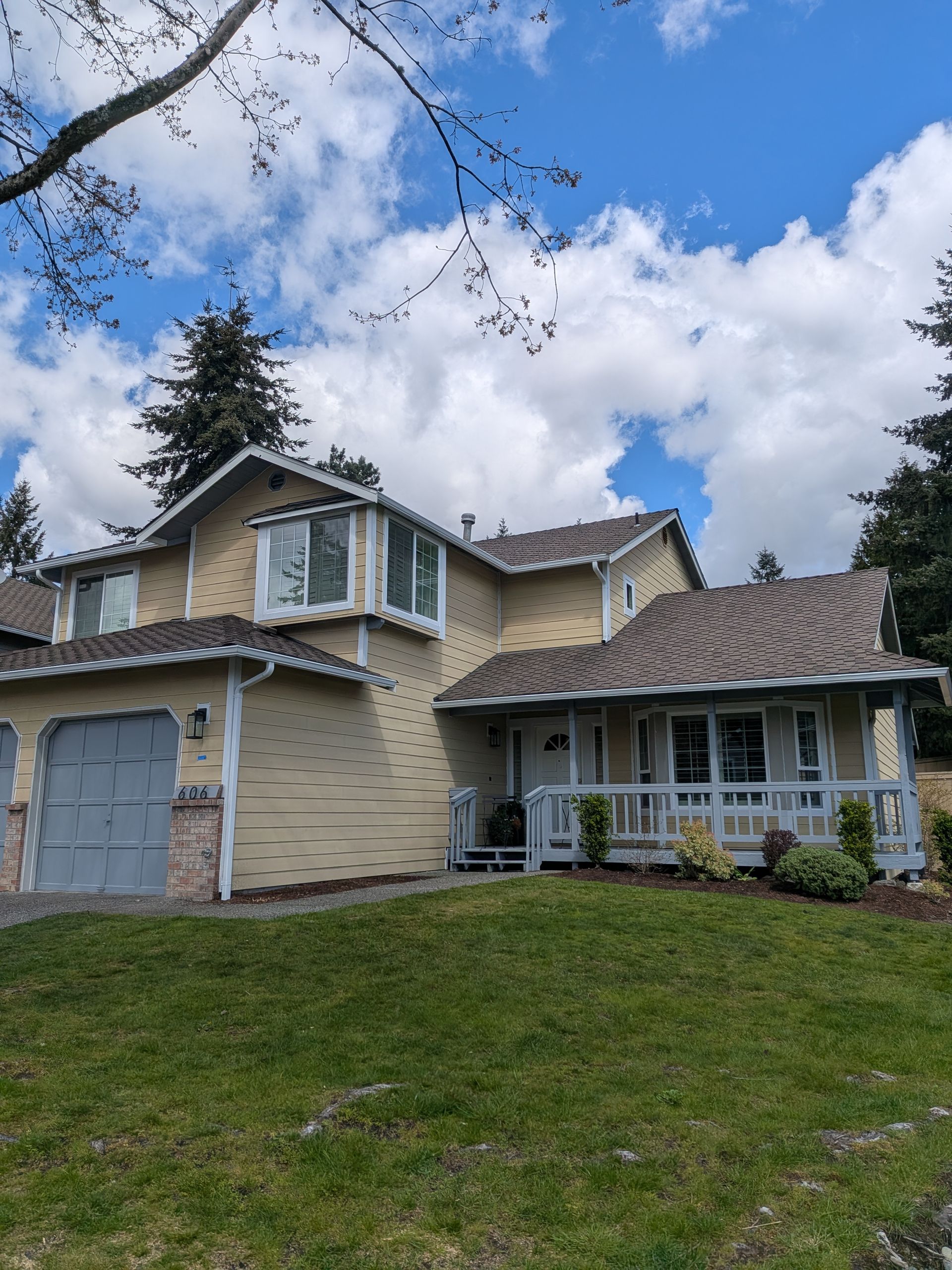 Two-story beige house with gray garage doors, white trim, and a grassy front yard under a cloudy sky