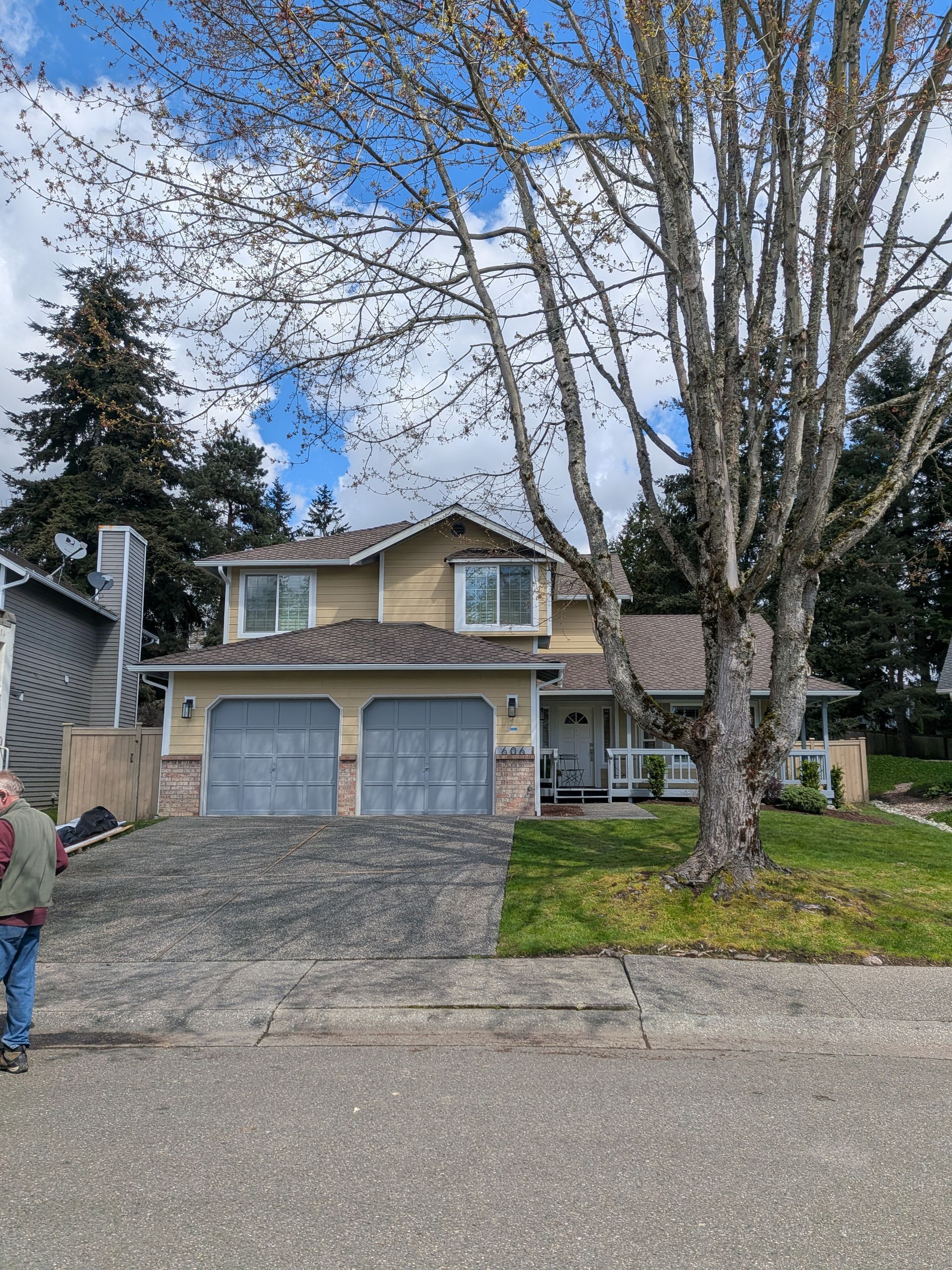 Suburban house with blue garage doors, large tree in front, and a child walking on the left