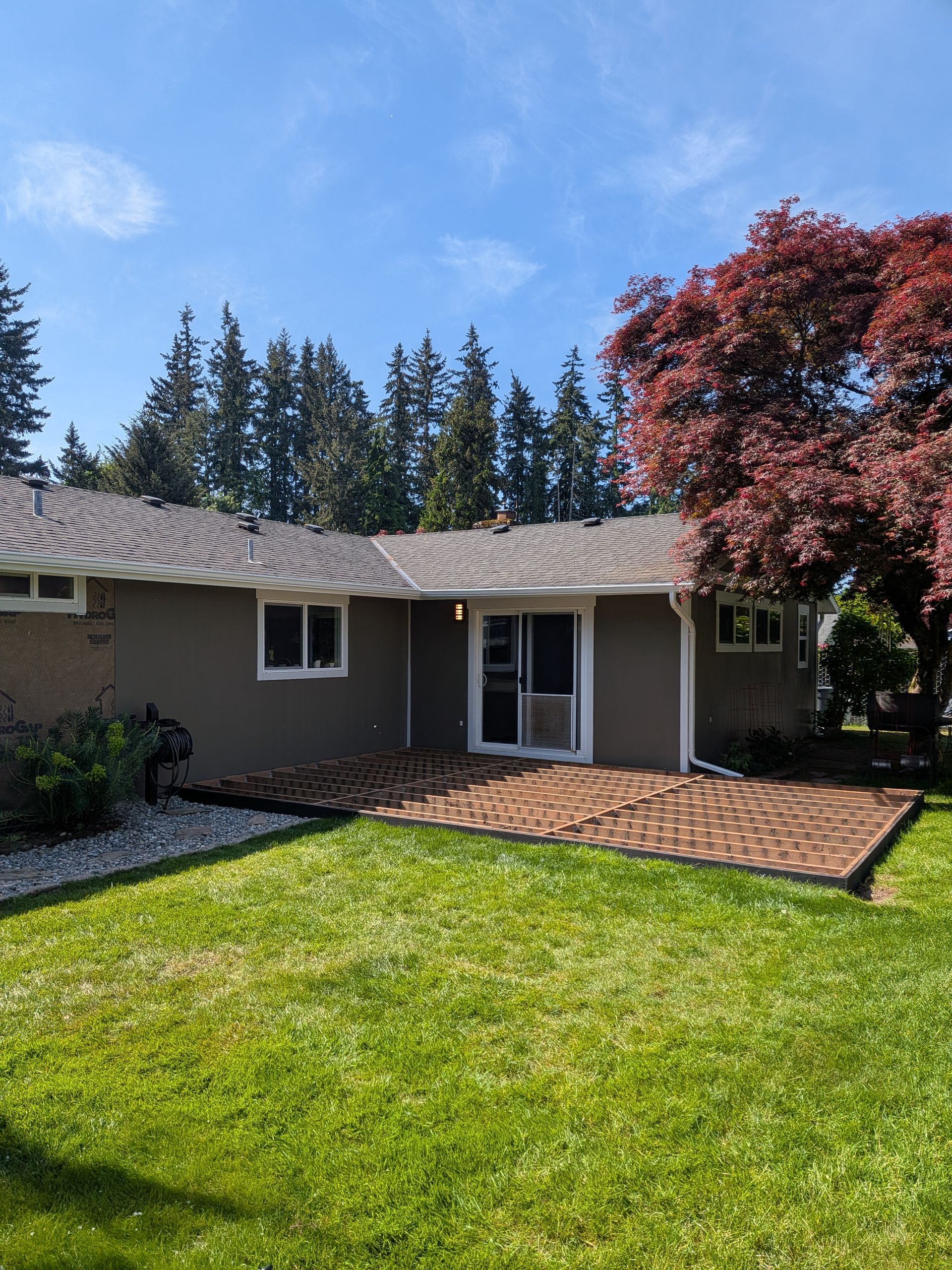 Single-story house with green lawn, brick patio, and a red tree under a blue sky.