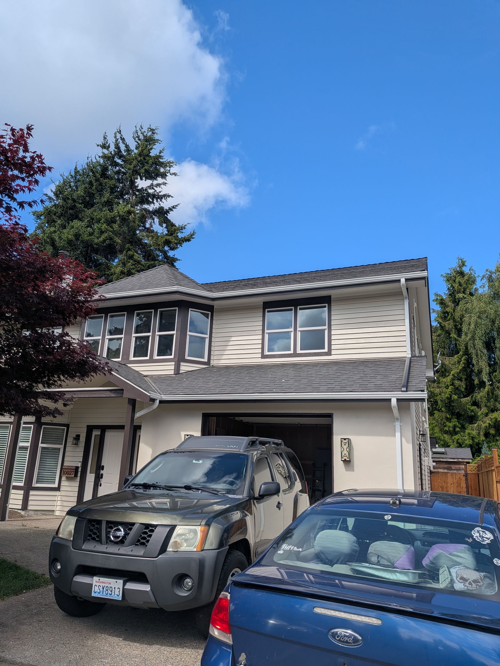 Two-story house with two parked cars under a blue sky and tree branches in front