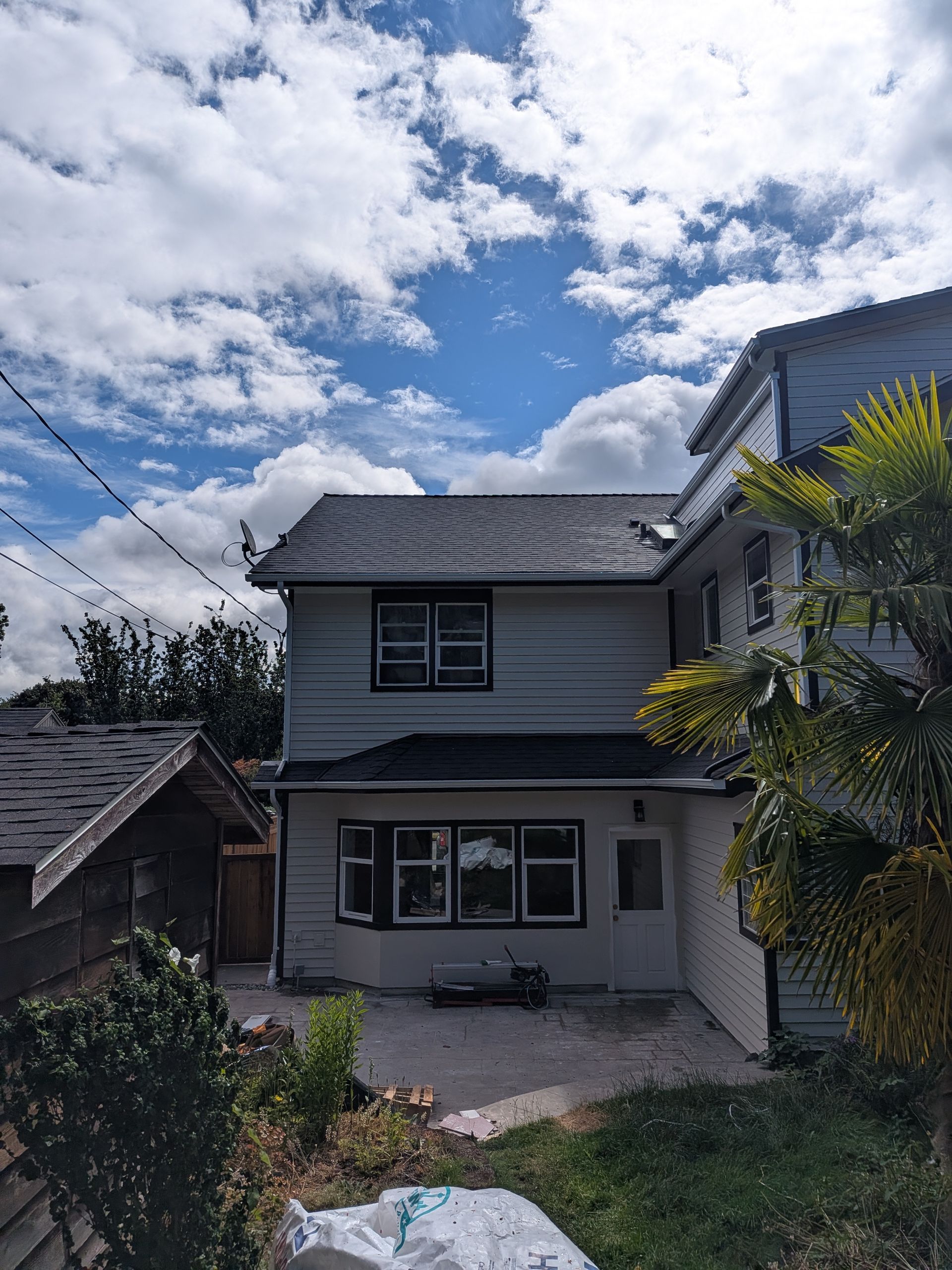 Two-story gray house with a small front yard under a cloudy blue sky