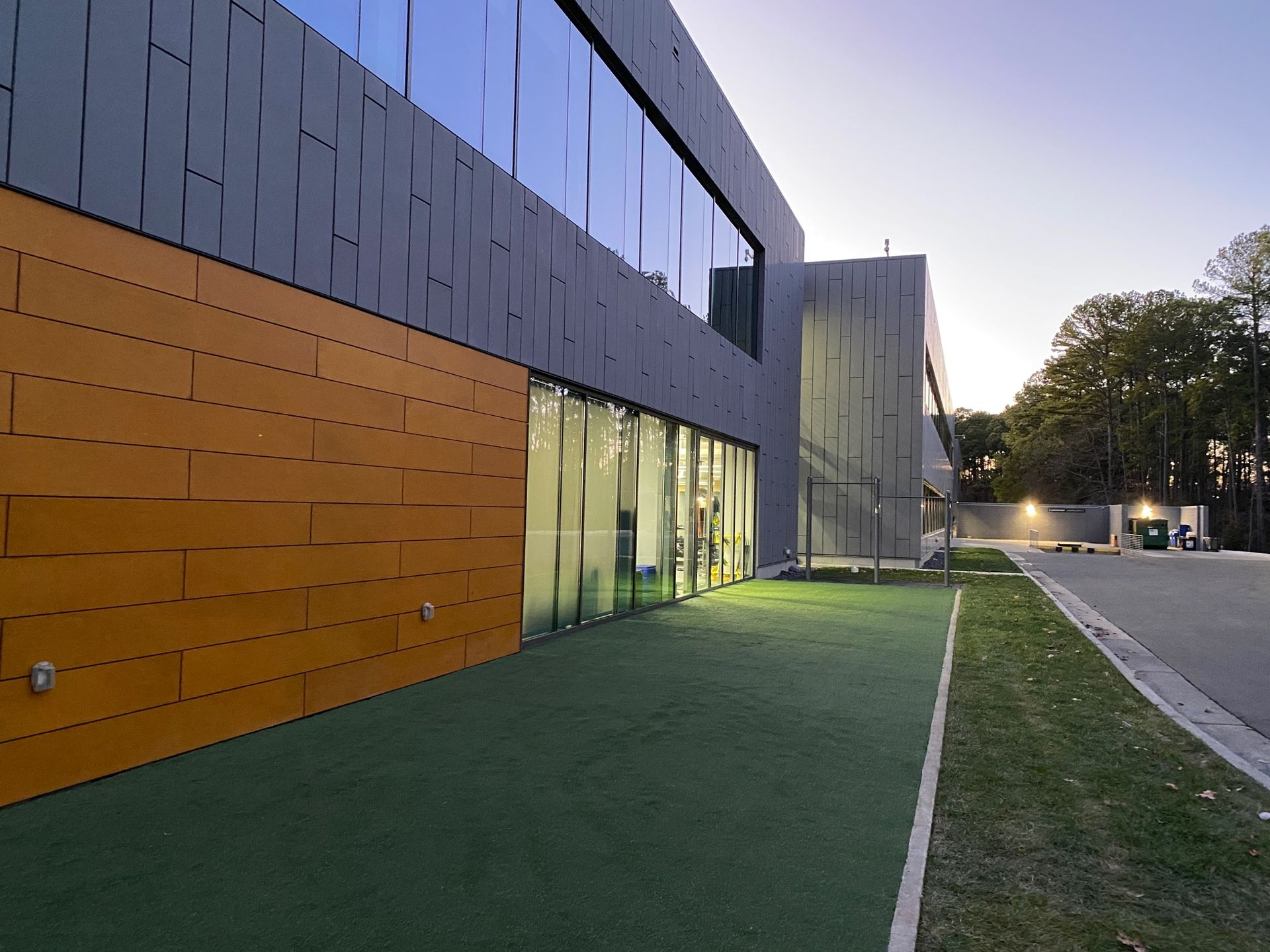 Modern building with orange and gray facade, glass windows, and artificial turf.