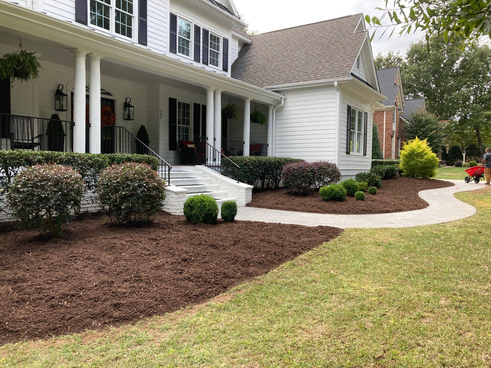 White house with porch, landscaping, and pathway with brown mulch.