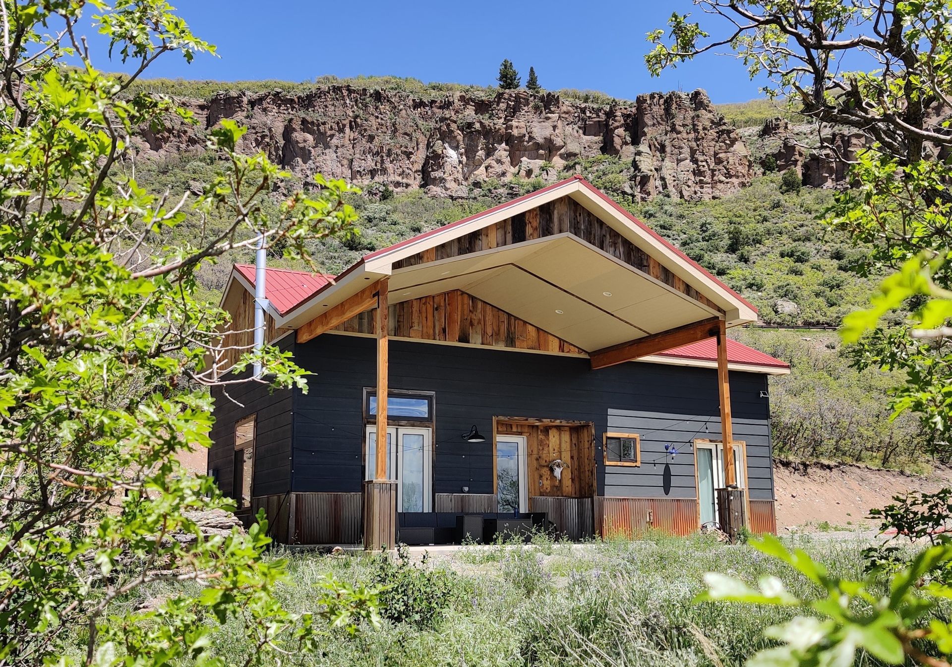 A small house with a red roof is surrounded by trees and grass. Maven Construction, Montrose, CO