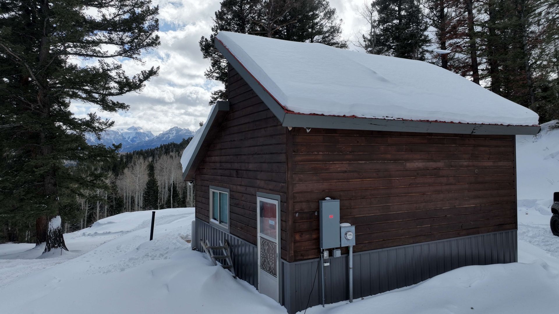 A small wooden house covered in snow with mountains in the background Maven Construction, Montrose, CO