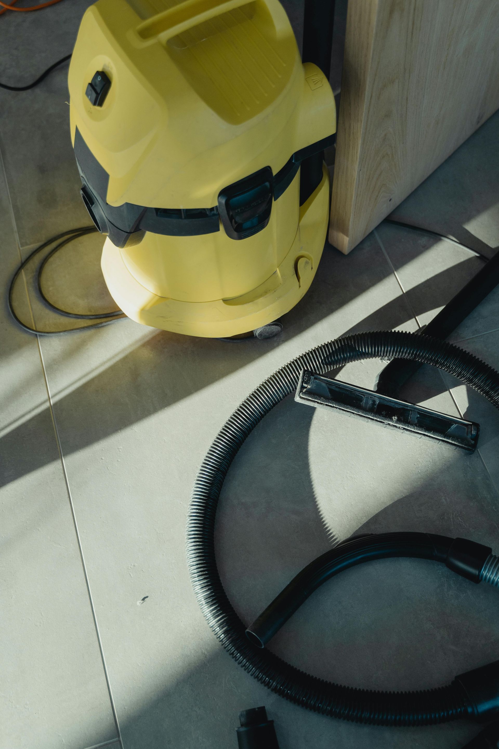 Yellow wet/dry vacuum with hose and attachment on gray tiled floor.
