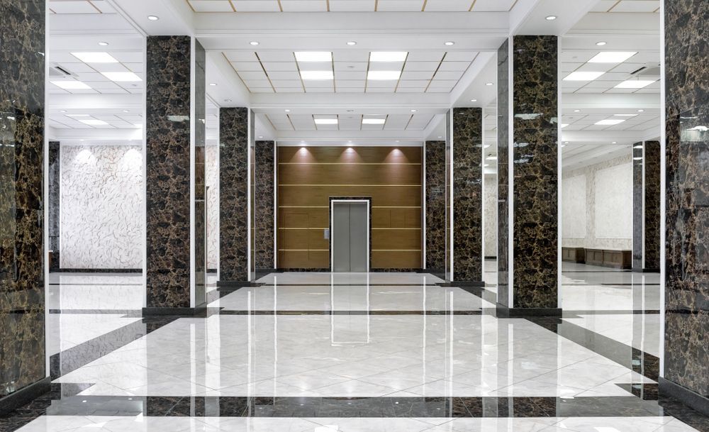 Elegant lobby with marble pillars and floors, a central elevator, and recessed lighting.