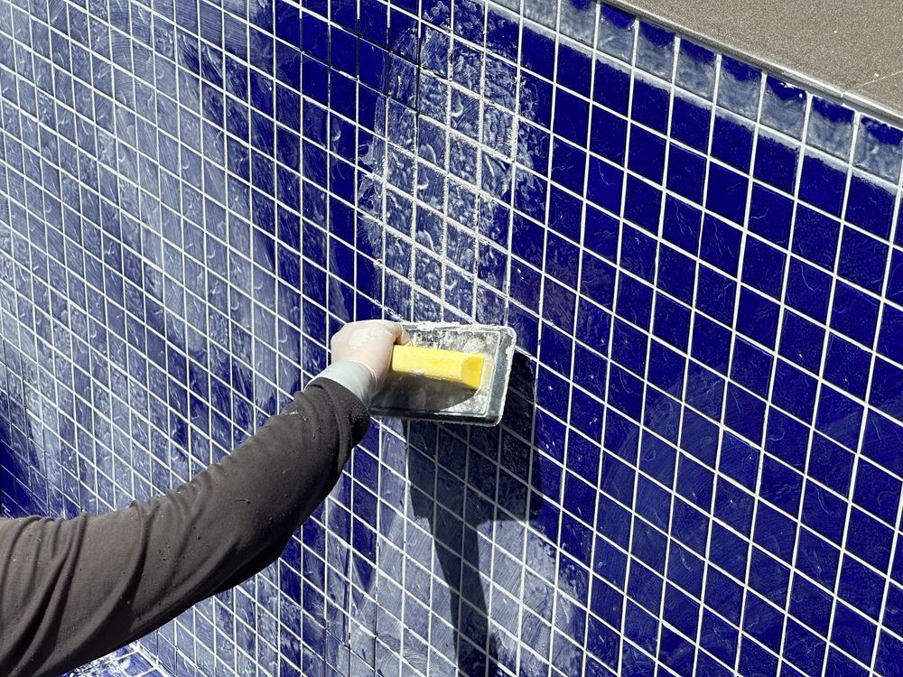 Person grouting blue tile on a pool wall using a yellow float tool.