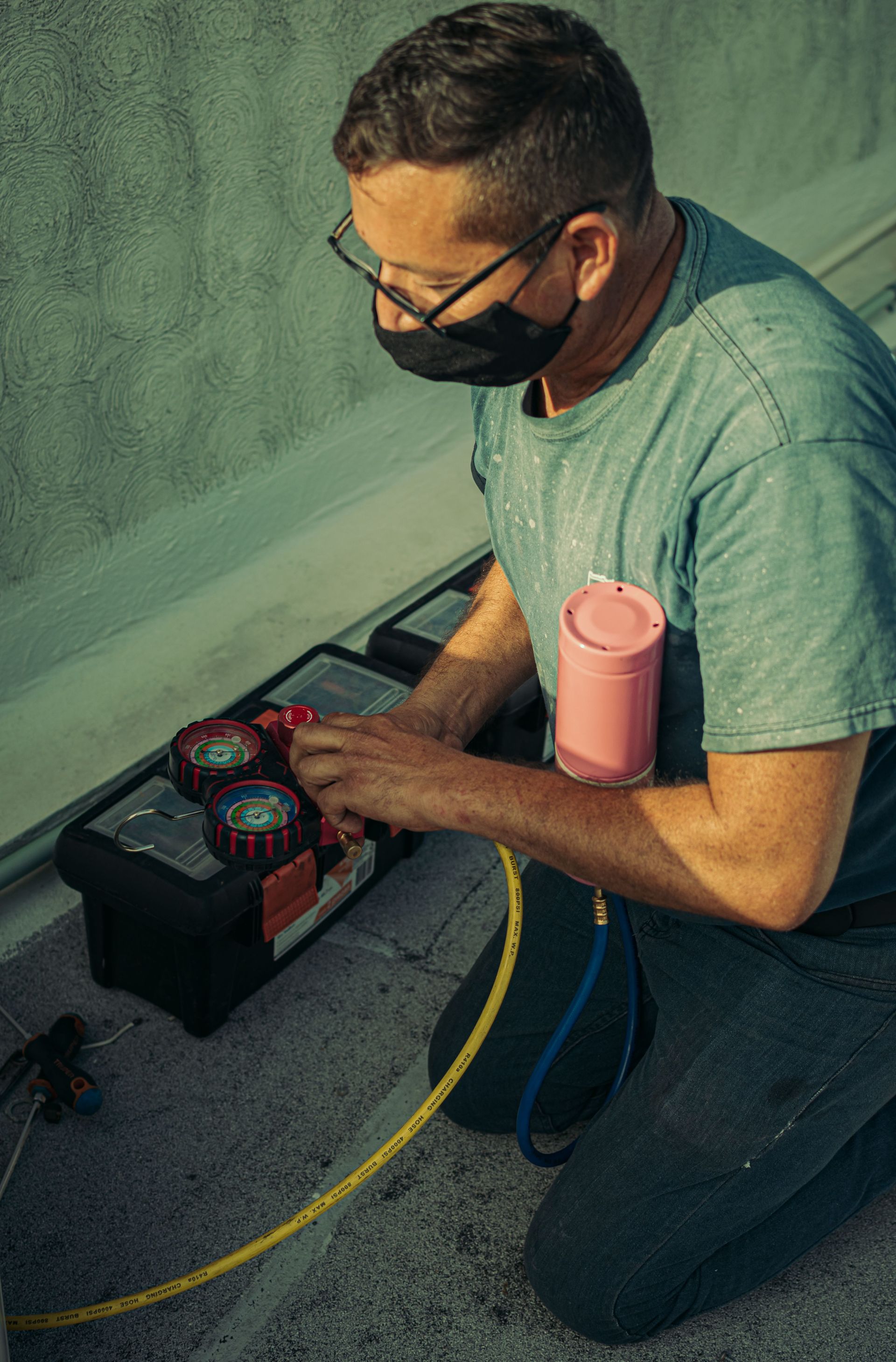 Person kneeling on a rooftop, inspecting an electrical tool and wiring beside a pink cup in daylight