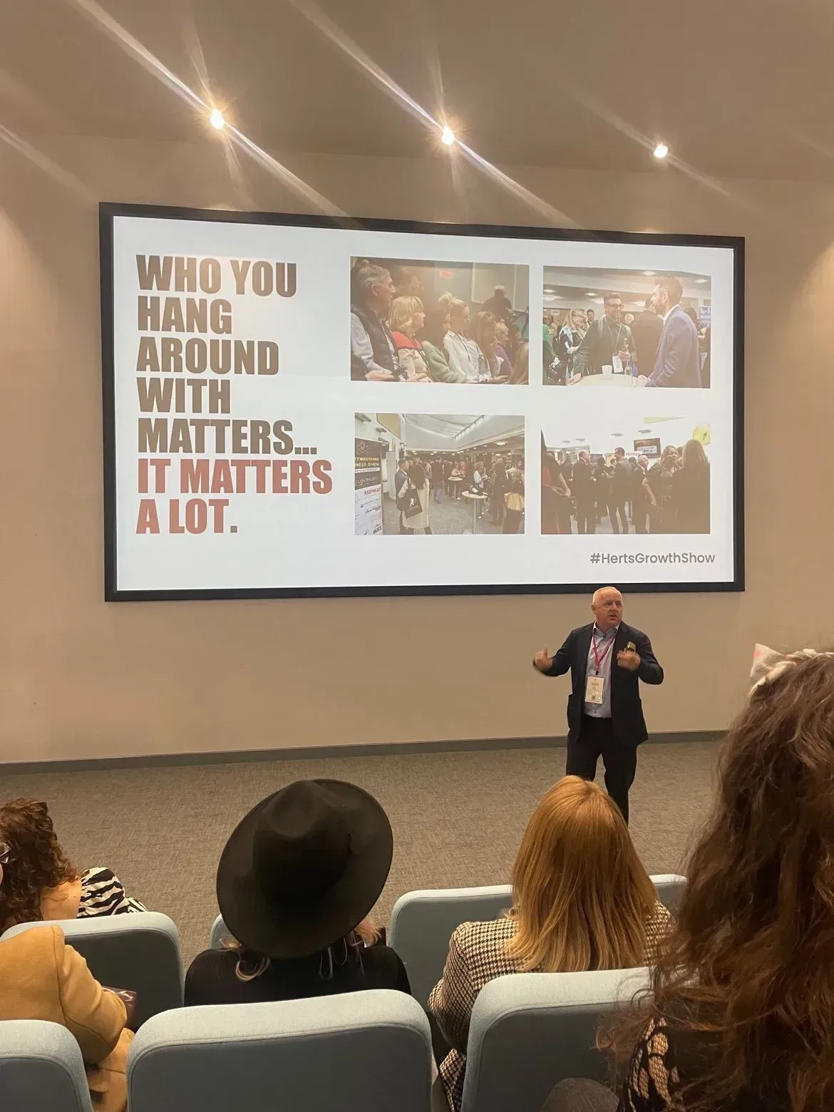 presenting to a seated audience with a slide reading: