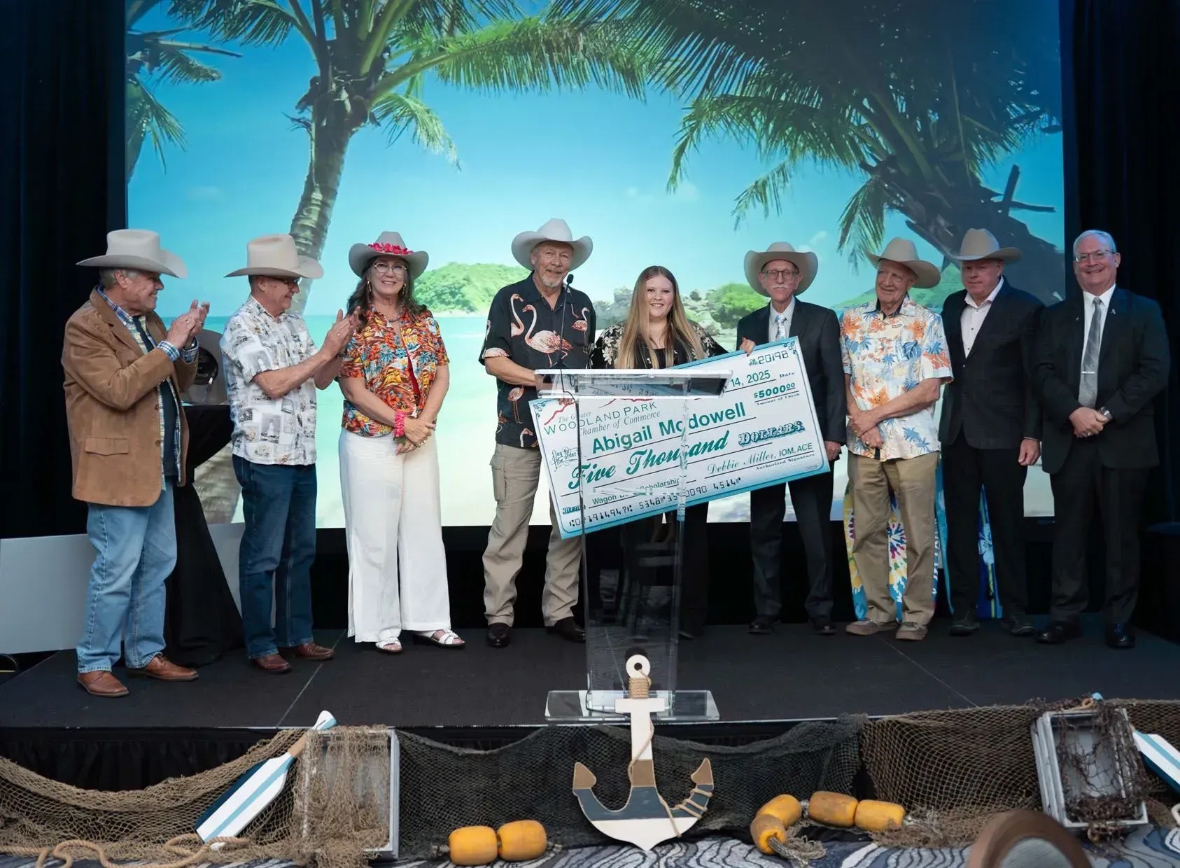 People on a stage holding a large check. They are wearing cowboy hats and tropical shirts.