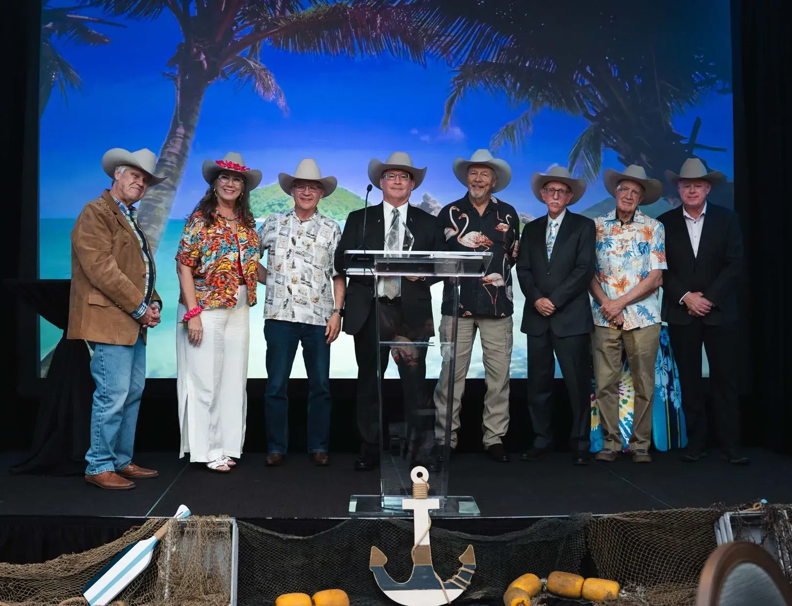 Group of people with cowboy hats and tropical shirts on a stage.