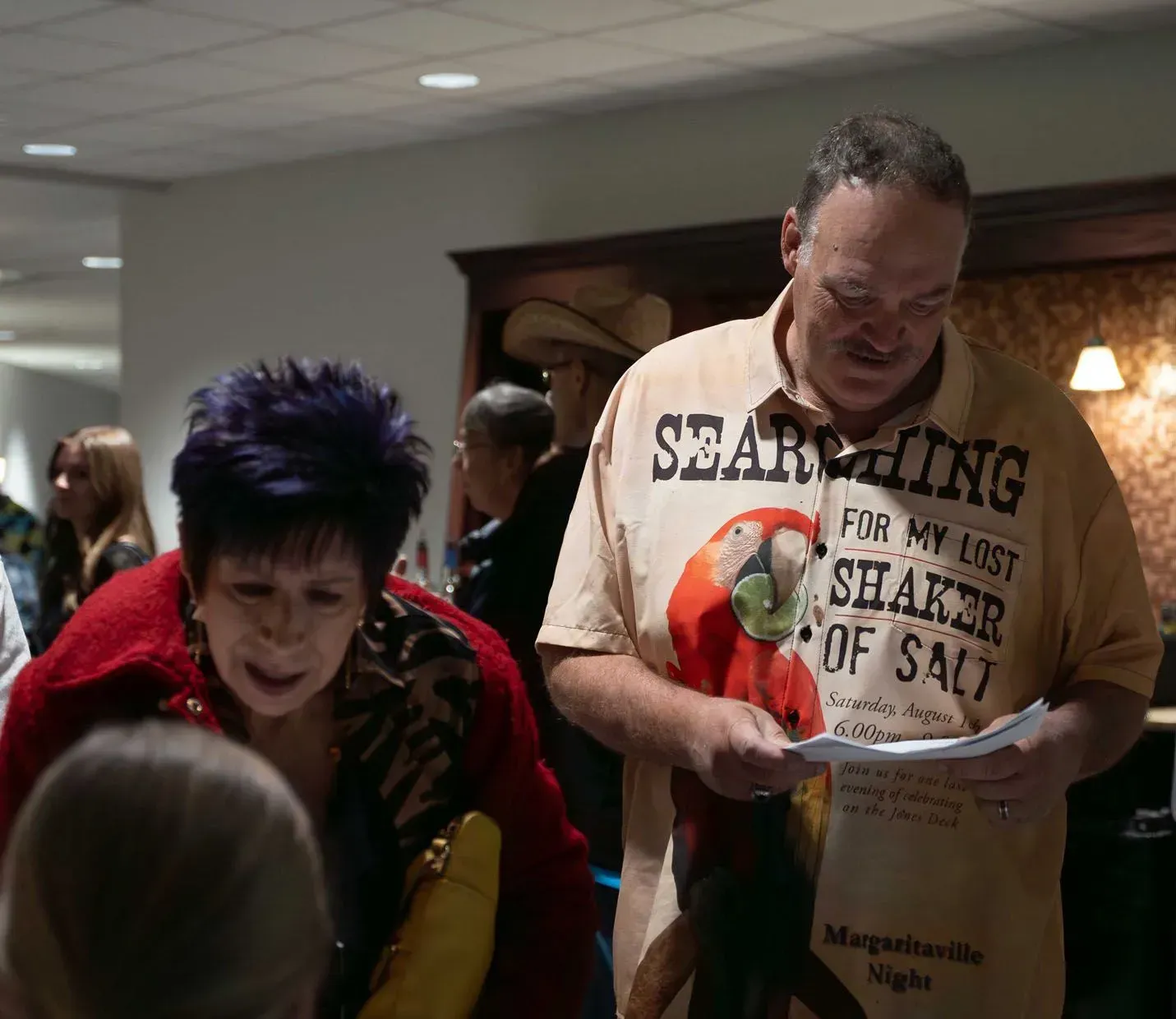 Woman with purple hair and man in a parrot shirt reading papers at an event.