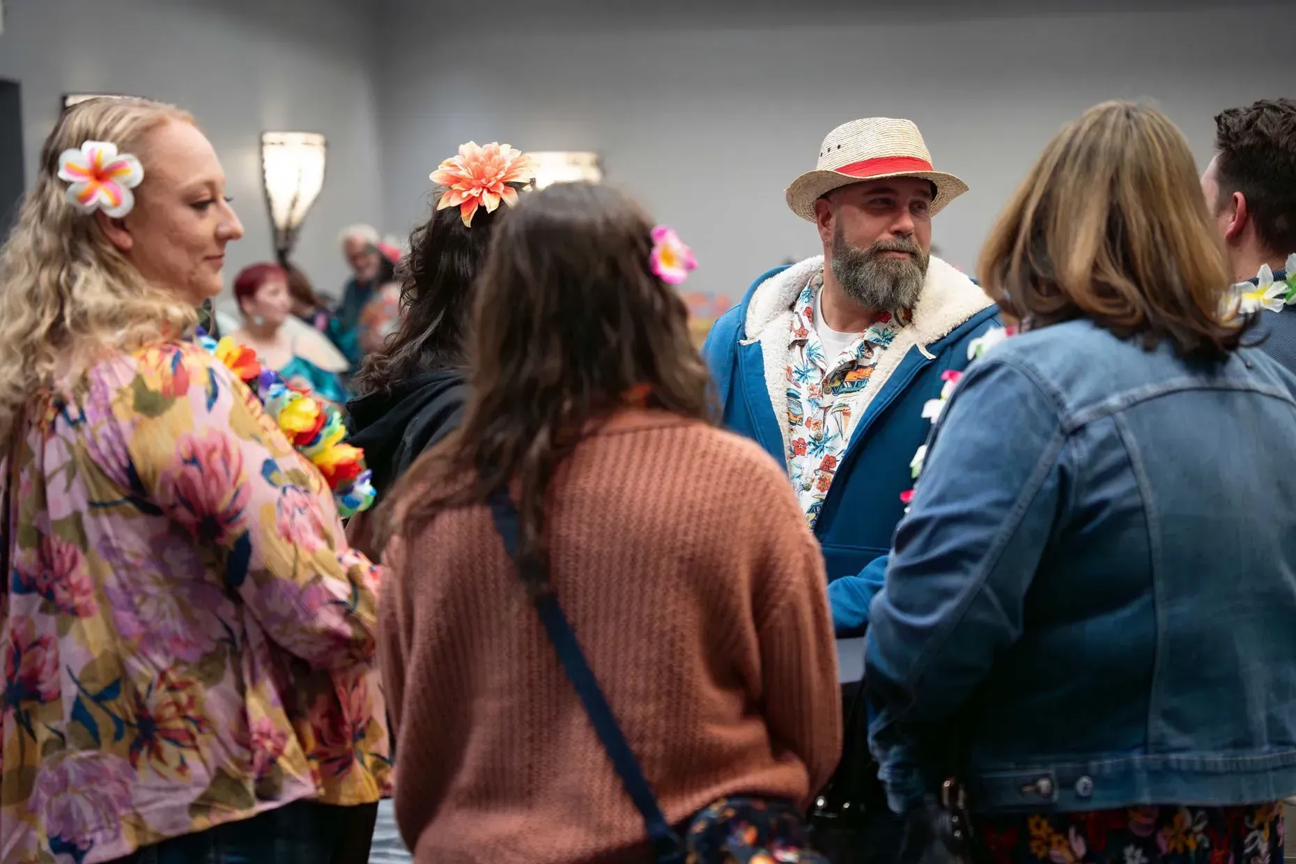 People in Hawaiian shirts and leis at a gathering; some wear flower hair accessories.