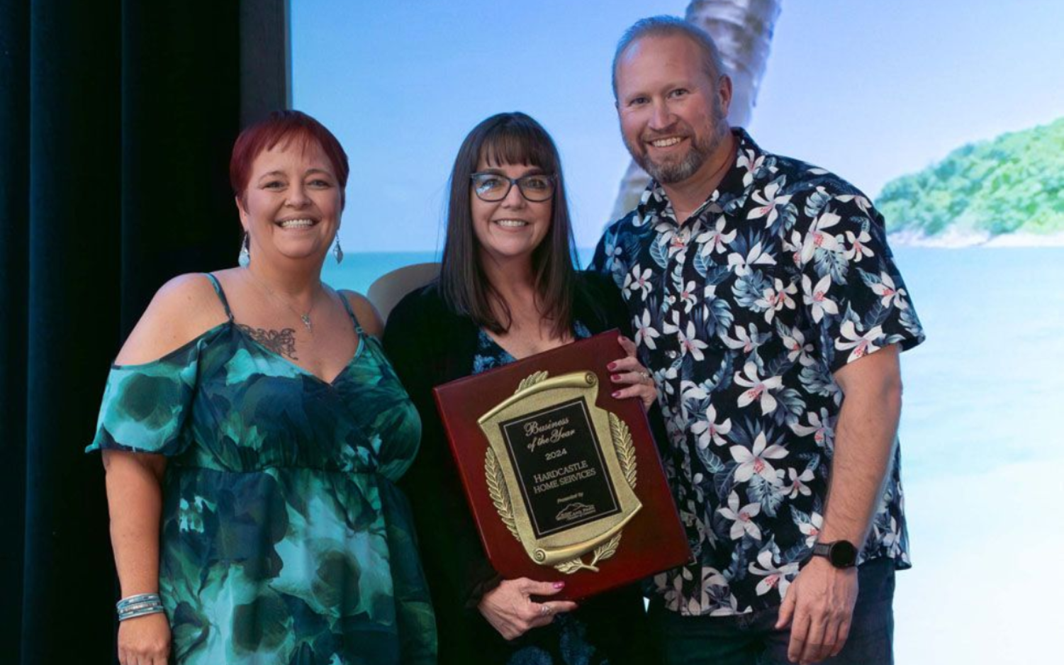 Two women accepting an award from a Man in a Flower shirt
