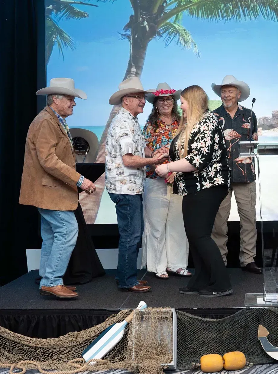 People on a stage, two men with cowboy hats and other people, being presented with an award at an event.