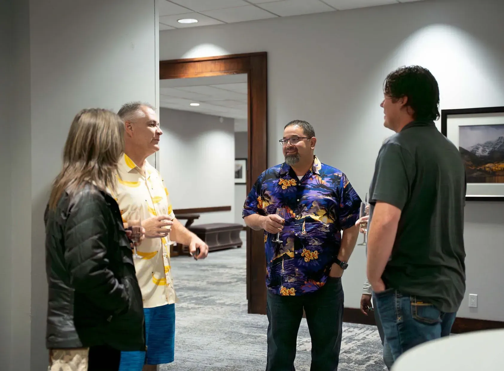 Four people talking in a hallway. One man in a Hawaiian shirt, another in yellow, blue shorts.