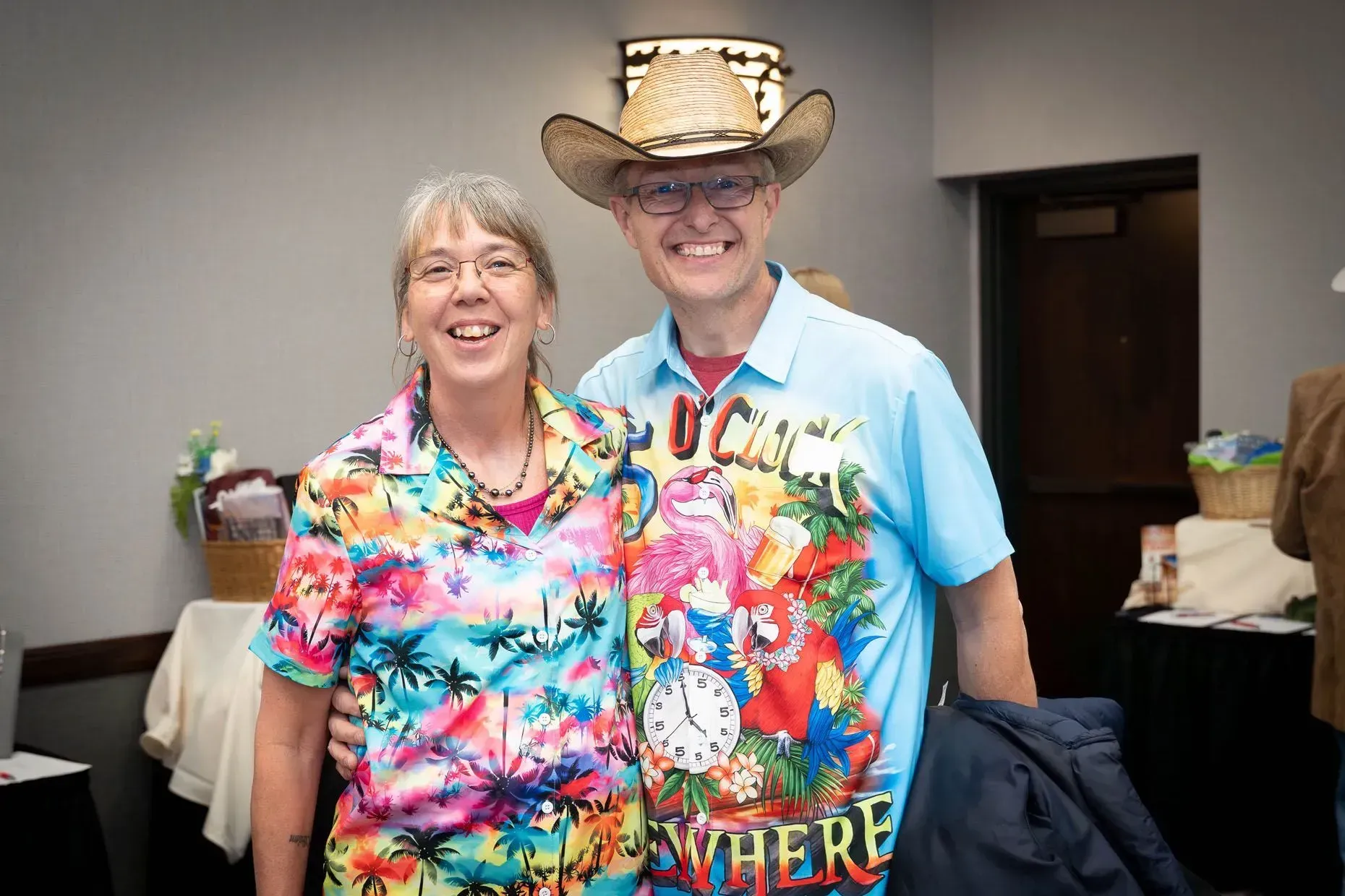 Smiling couple in tropical shirts pose indoors, man in cowboy hat.
