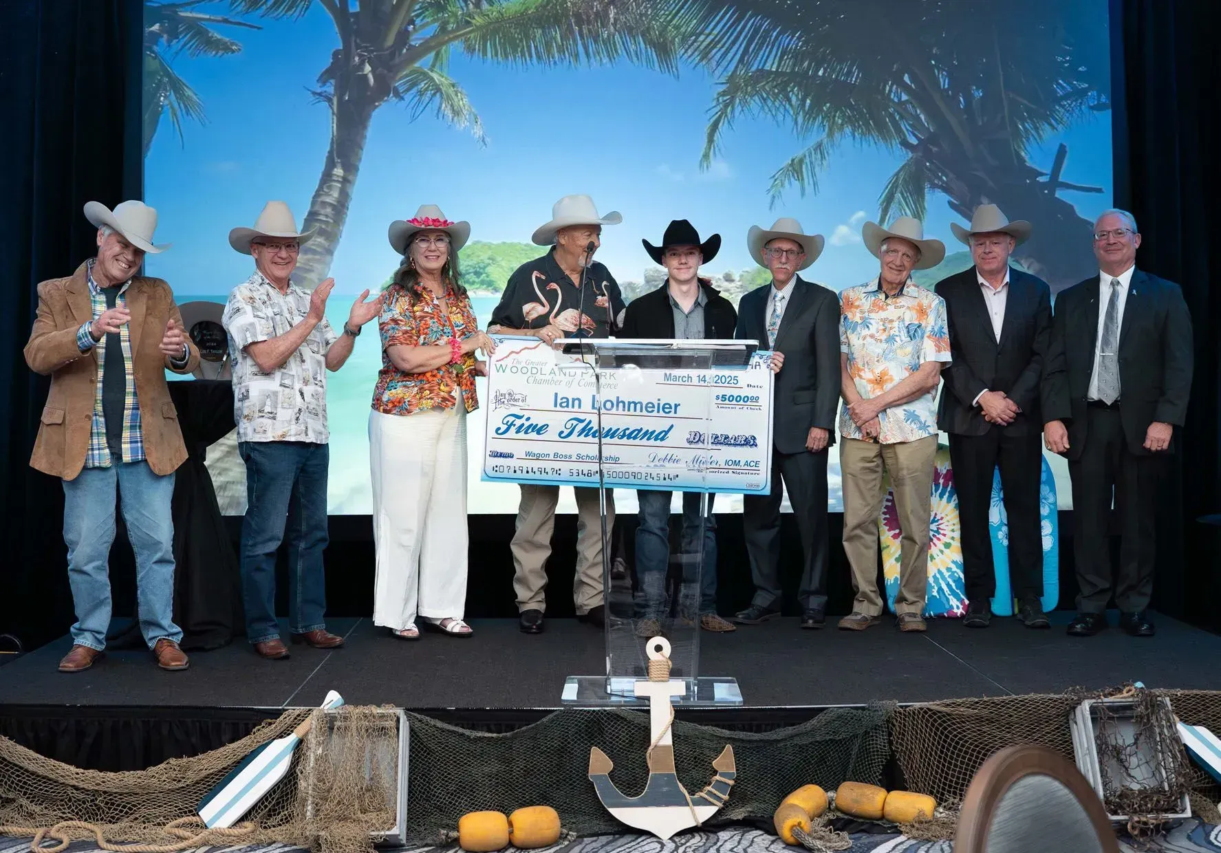 People in cowboy hats holding oversized check on stage with ocean backdrop.