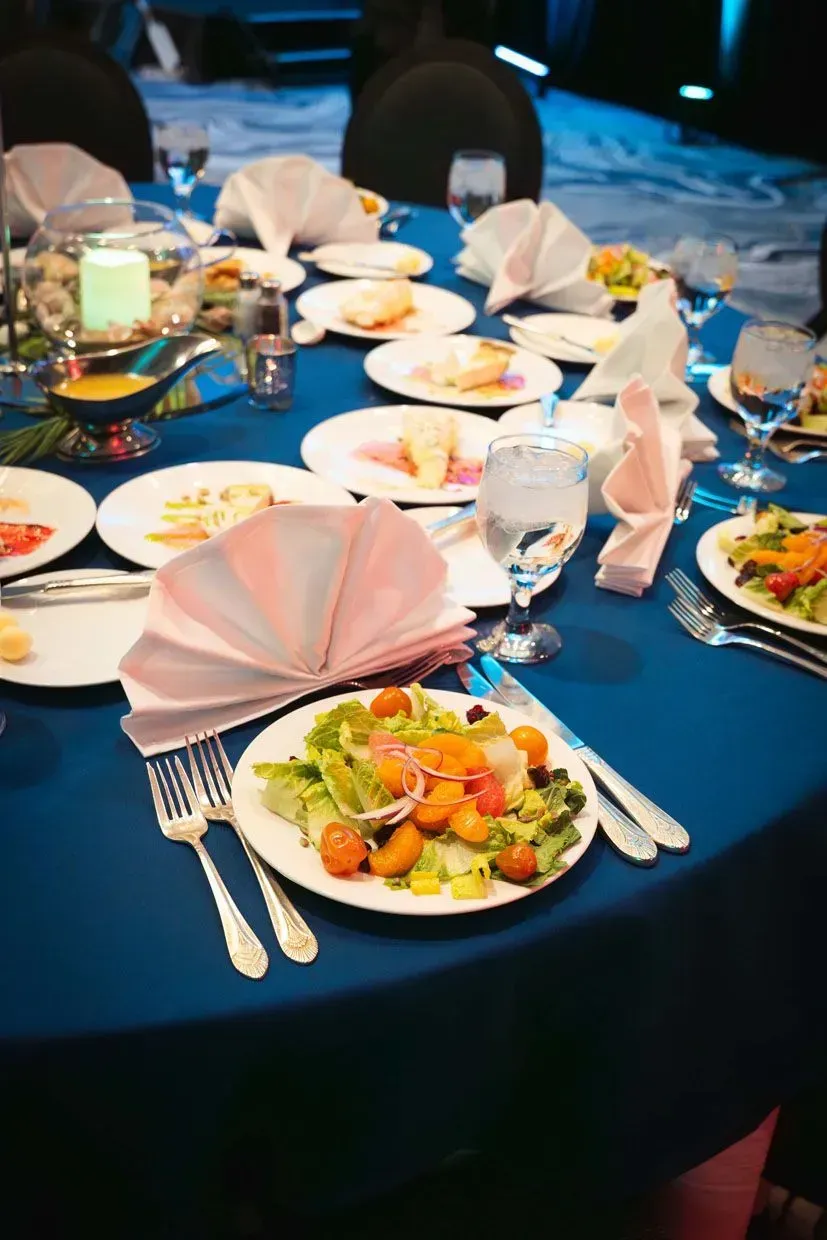 A formal dinner table with blue tablecloth, salads, folded napkins, and glasses.