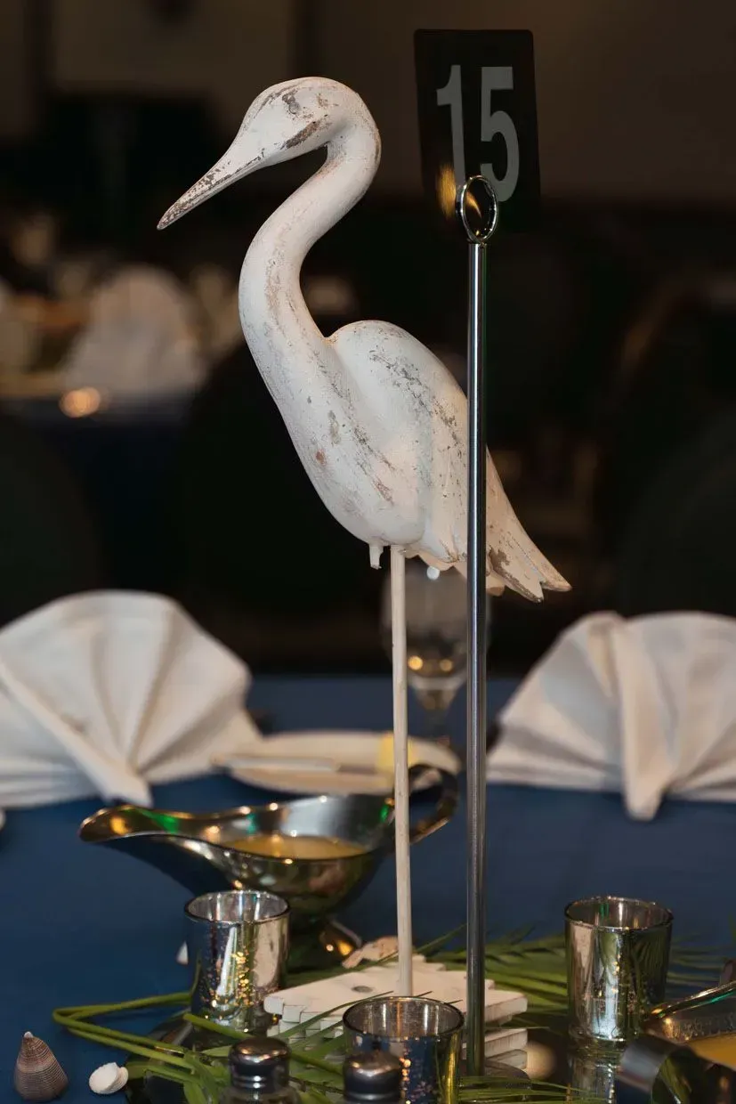 White heron table centerpiece with a number 15, set on a blue tablecloth at a dining table.