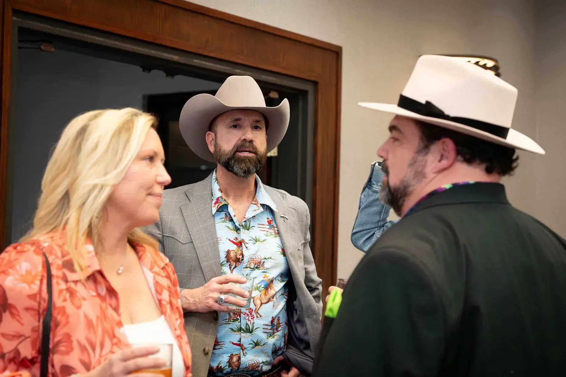 Three people in a social gathering, one wearing a cowboy hat, others in stylish casual attire, indoors.