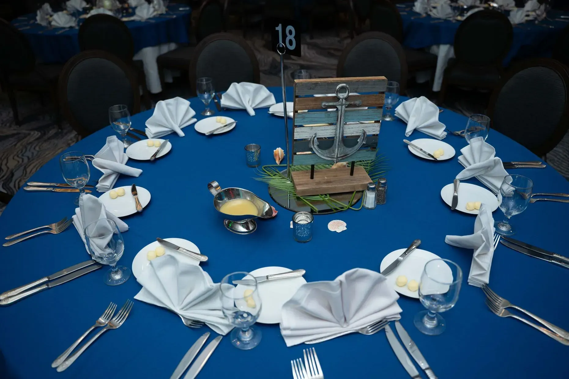 Round table set for a nautical-themed event, blue tablecloth, napkins folded as fans.