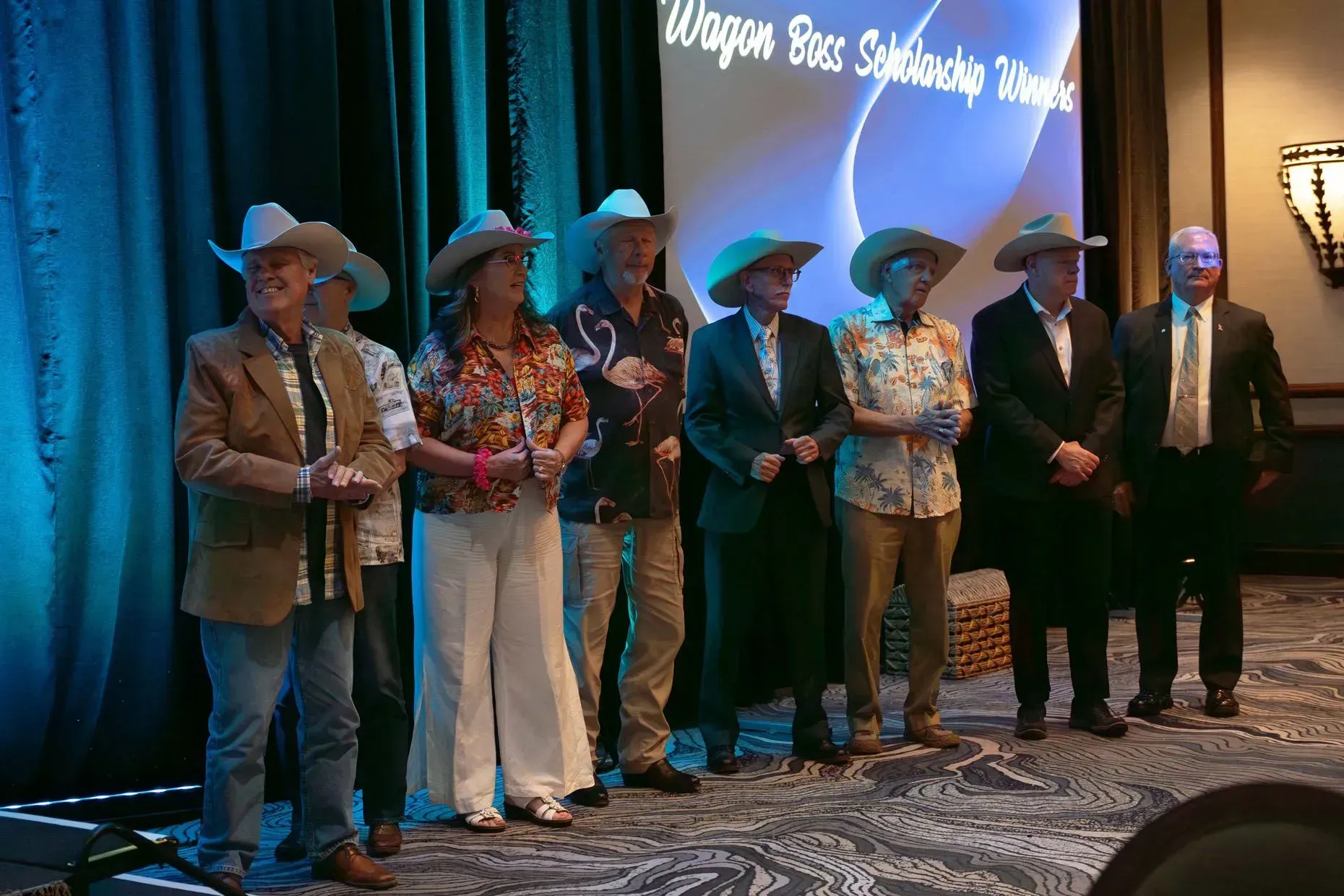 Group of seven people wearing cowboy hats onstage at an event.