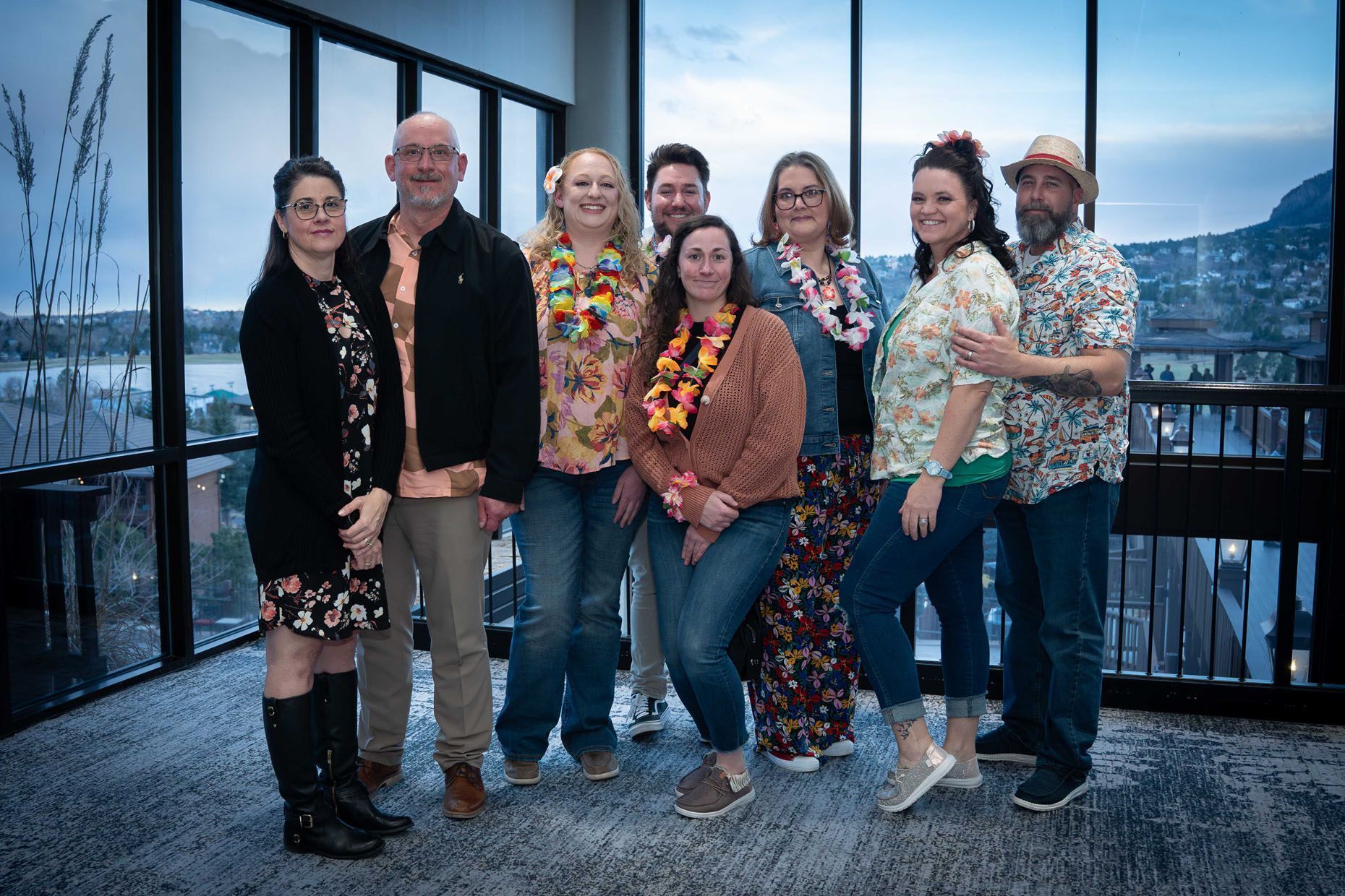 Group of people in casual attire, some with leis, posing indoors with a scenic view.