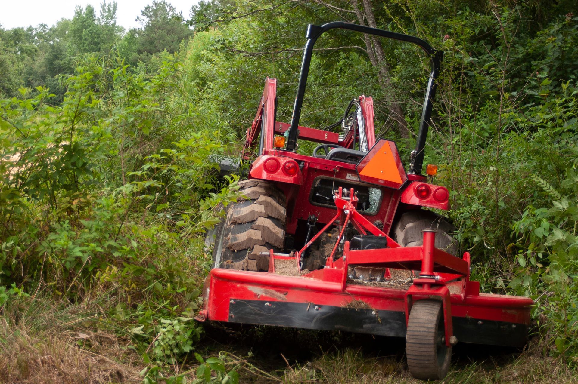 Red forestry mulcher tractor clearing brush in a wooded area