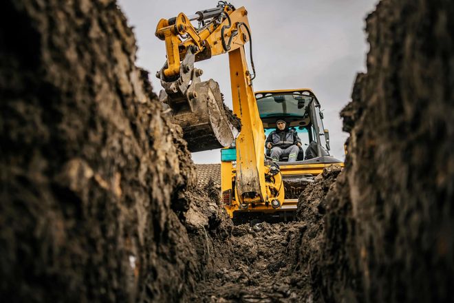 Yellow excavator digging a trench between muddy earth walls