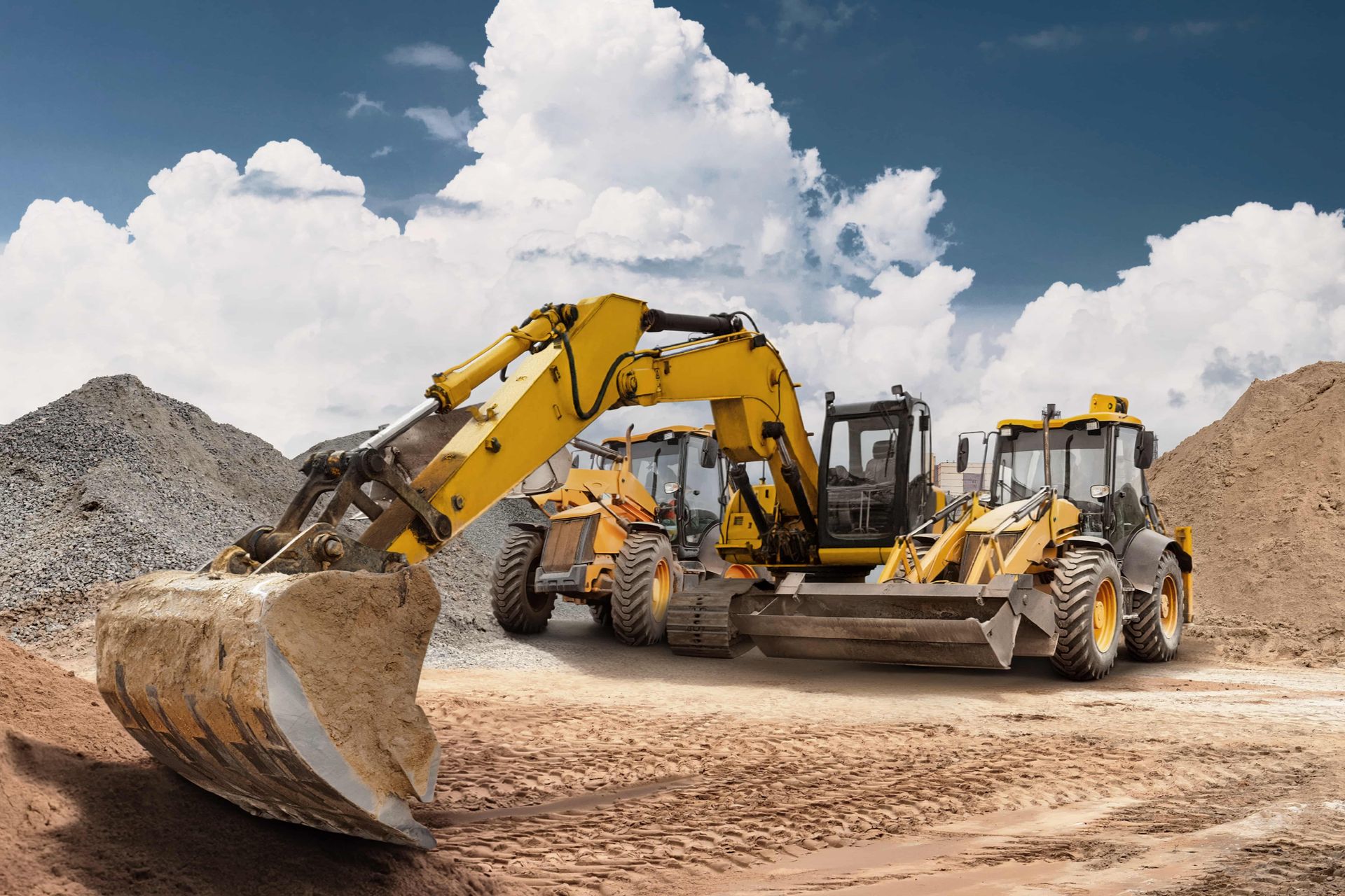 Yellow excavators and a bulldozer on a dirt construction site under a cloudy sky