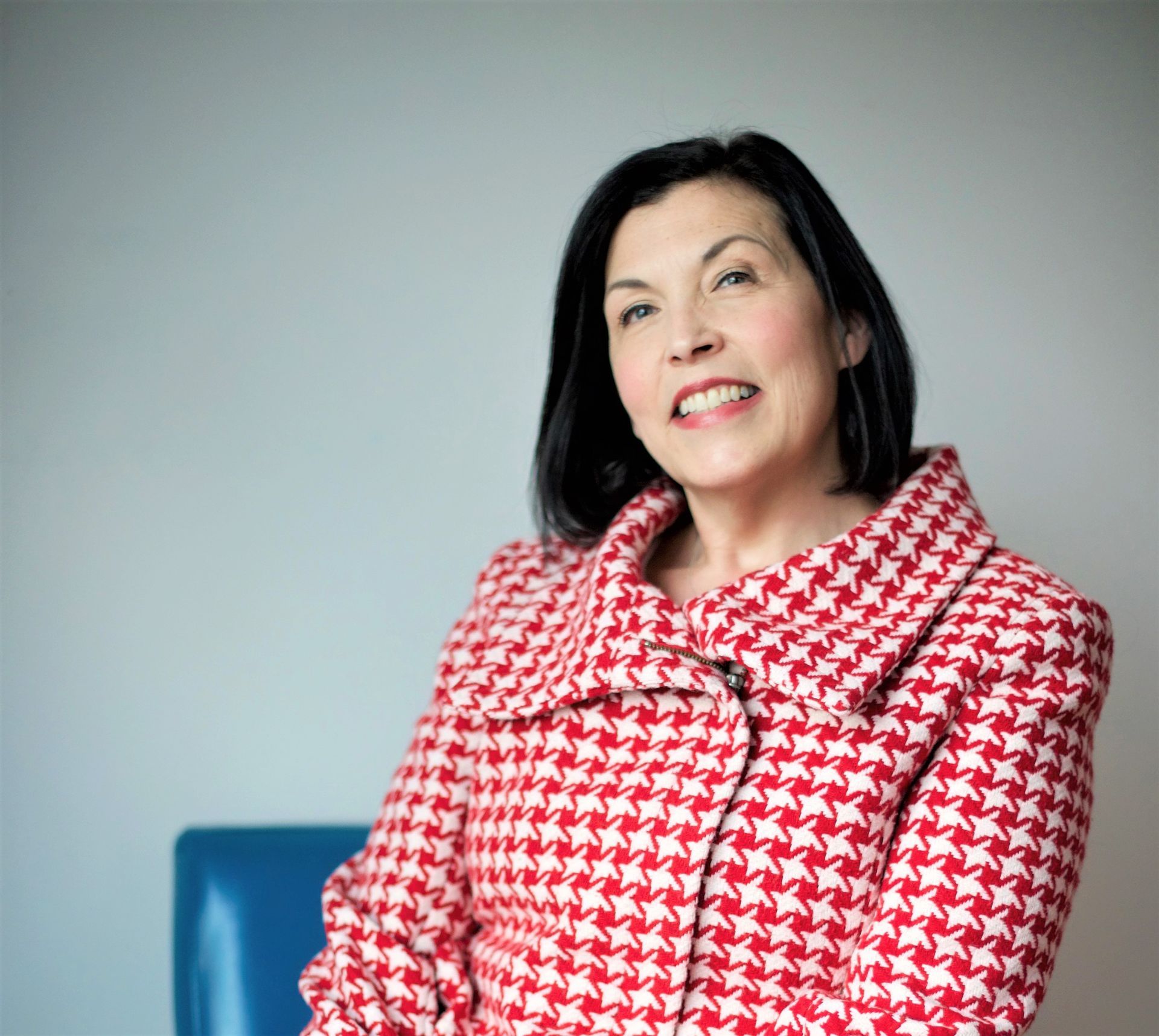 Owner Cathy Von Eschen in a red and white coat is sitting in a chair and smiling.