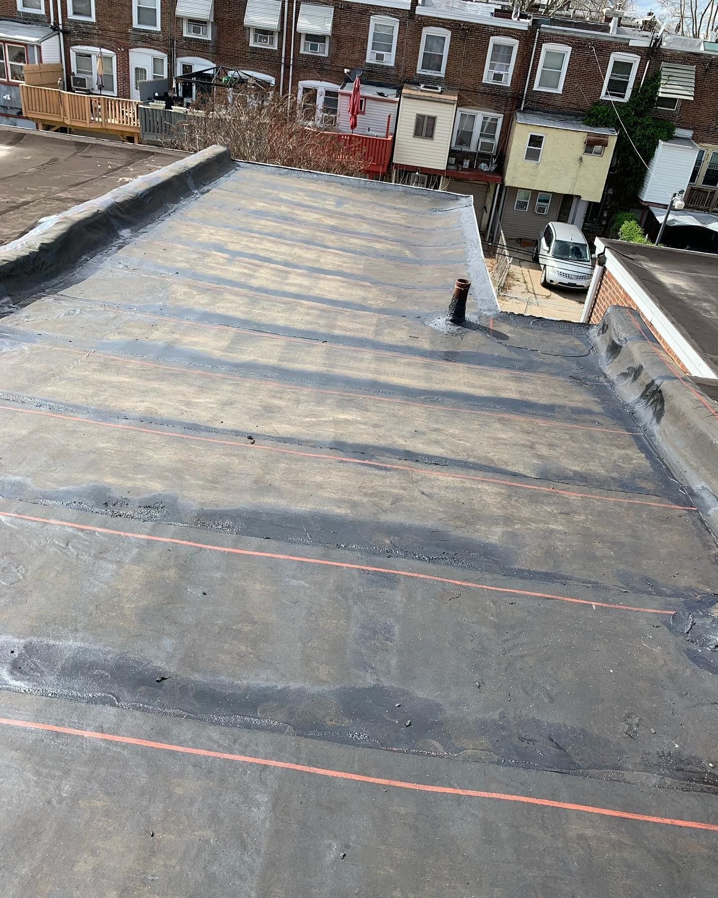 Rooftop with tar paper strips and a worker near the center, viewed from above.