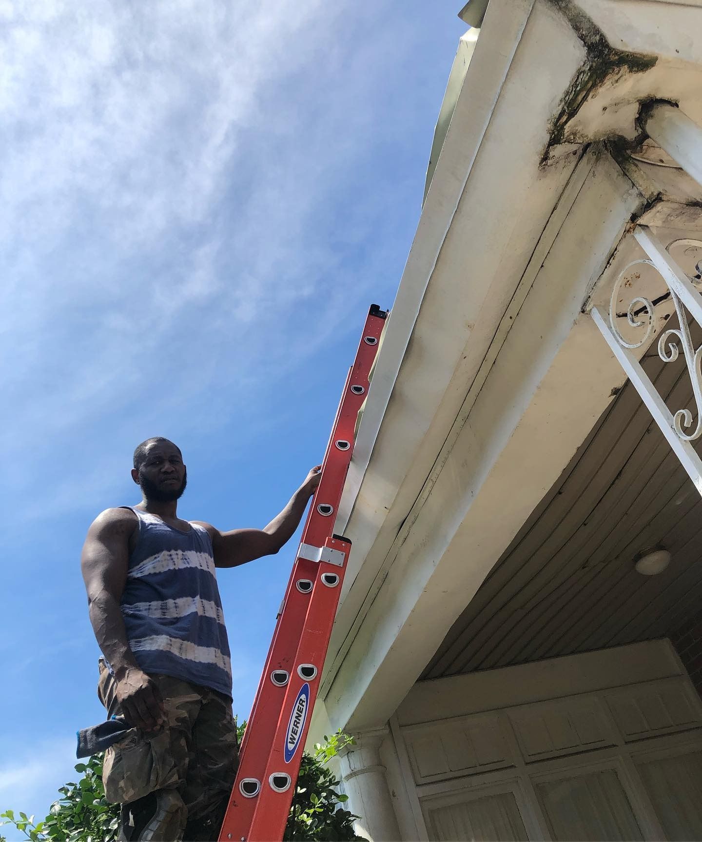 Man on a red ladder repairing white house gutters under a blue sky